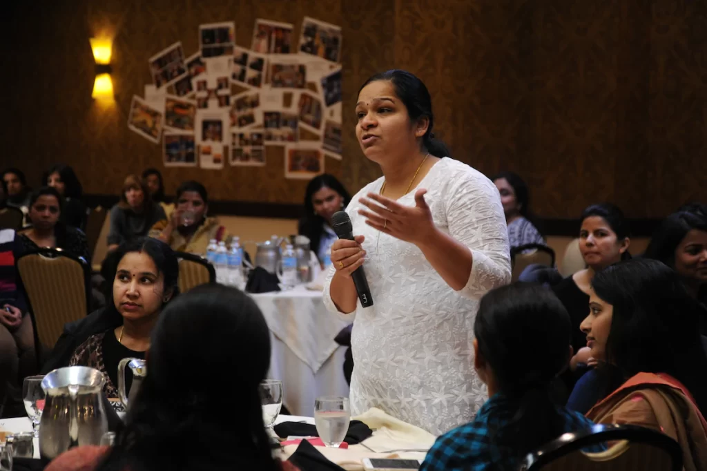 Woman with microphone speaks infant of room full of women